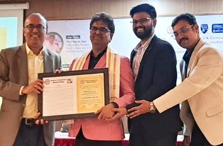 Four men are standing and smiling indoors in a conference room.