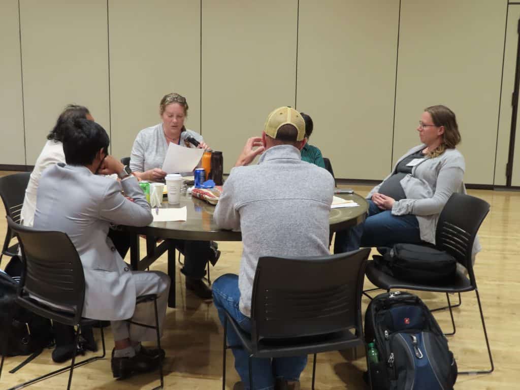Six people sit around a round table in a meeting room, engaged in discussion at the BioWRAP 2025 Annual Meeting. Papers, drinks, and snacks are on the table. The setting appears casual and collaborative. - BioWRAP