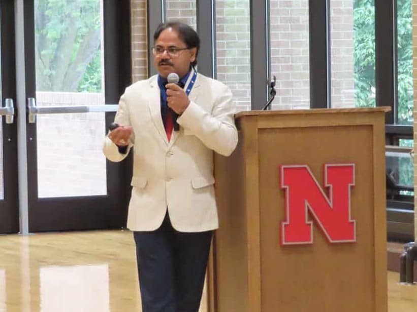 A man in a white blazer speaks into a microphone beside a podium with a large red "N" logo during the 2025 Annual Meeting in a bright room with large windows and wooden floors. - BioWRAP