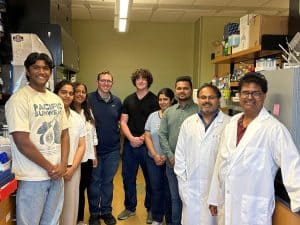 A group of nine people, some in lab coats, stand and smile together in a South Dakota Mines laboratory filled with shelves, equipment, and supplies—highlighting the power of mentorship through the Pyramid Approach. - BioWRAP